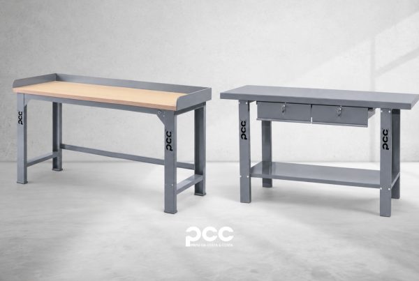 Duas bancadas de trabalho PCC para oficina, uma com tampo em madeira e outra com duas gavetas e prateleira inferior, com estrutura metálica cinzenta.